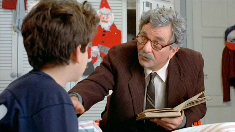 Still from The Princess Bride. Peter Falk holds a book at Fred Savage's bedside, leaning forward while speaking to him.
