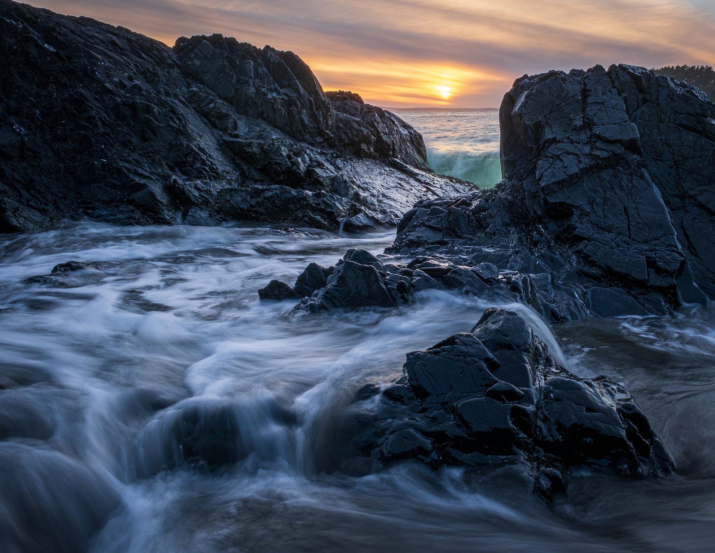 Rocks at sunset creating a small tide pool, photographed low to the ground and at a long exposure.