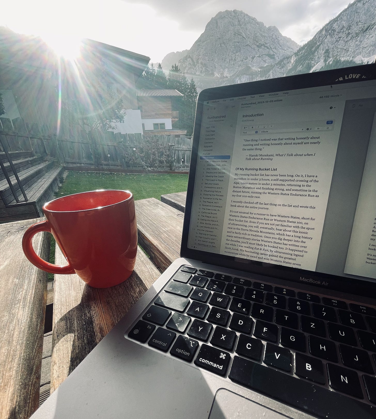 The author's macbook on a table with mountains in the background and a coffee mug