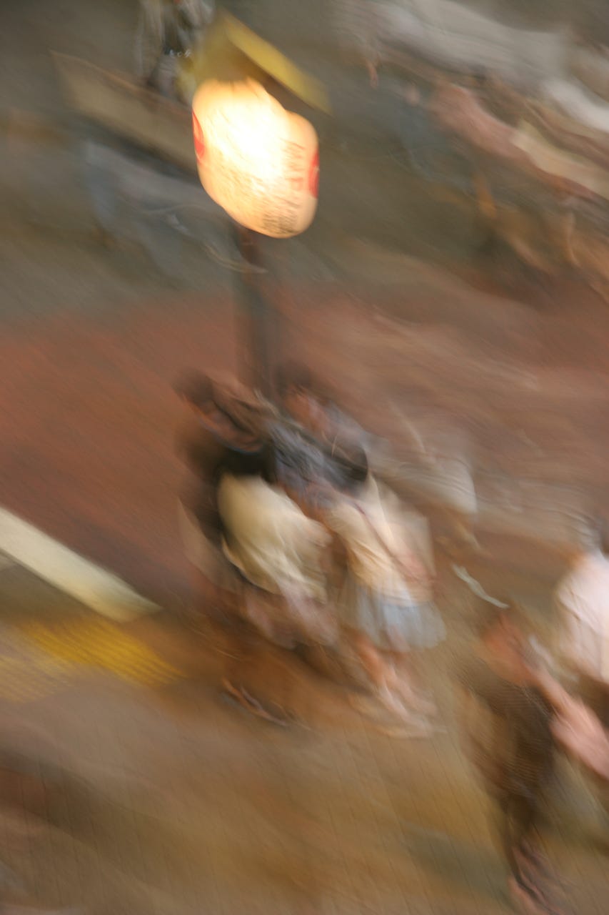 A blurry image of people standing on a street

Description automatically generated
