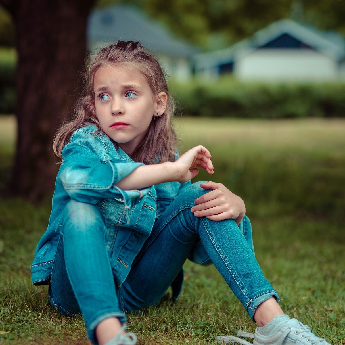 Little girl with blue eyes, sitting on grass and gazing wistfully