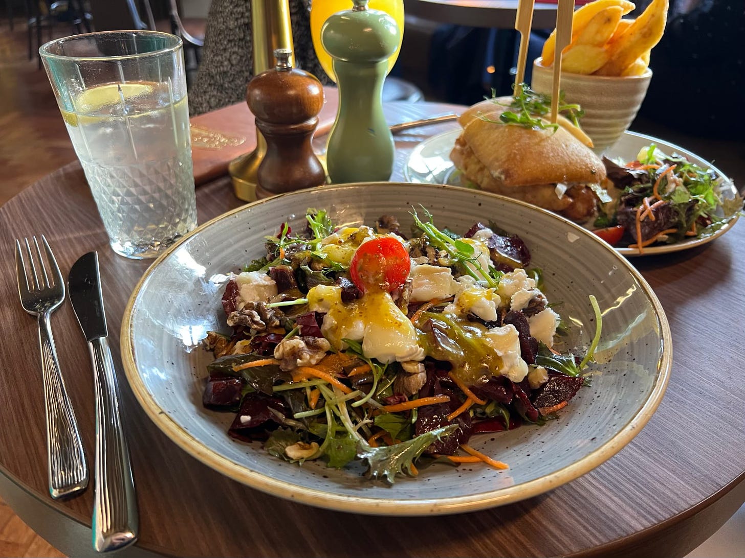 A goat’s cheese salad with beetroot and butternut squash is sat on a pub table next to a posh fish finger sarnie and a couple of drinks.