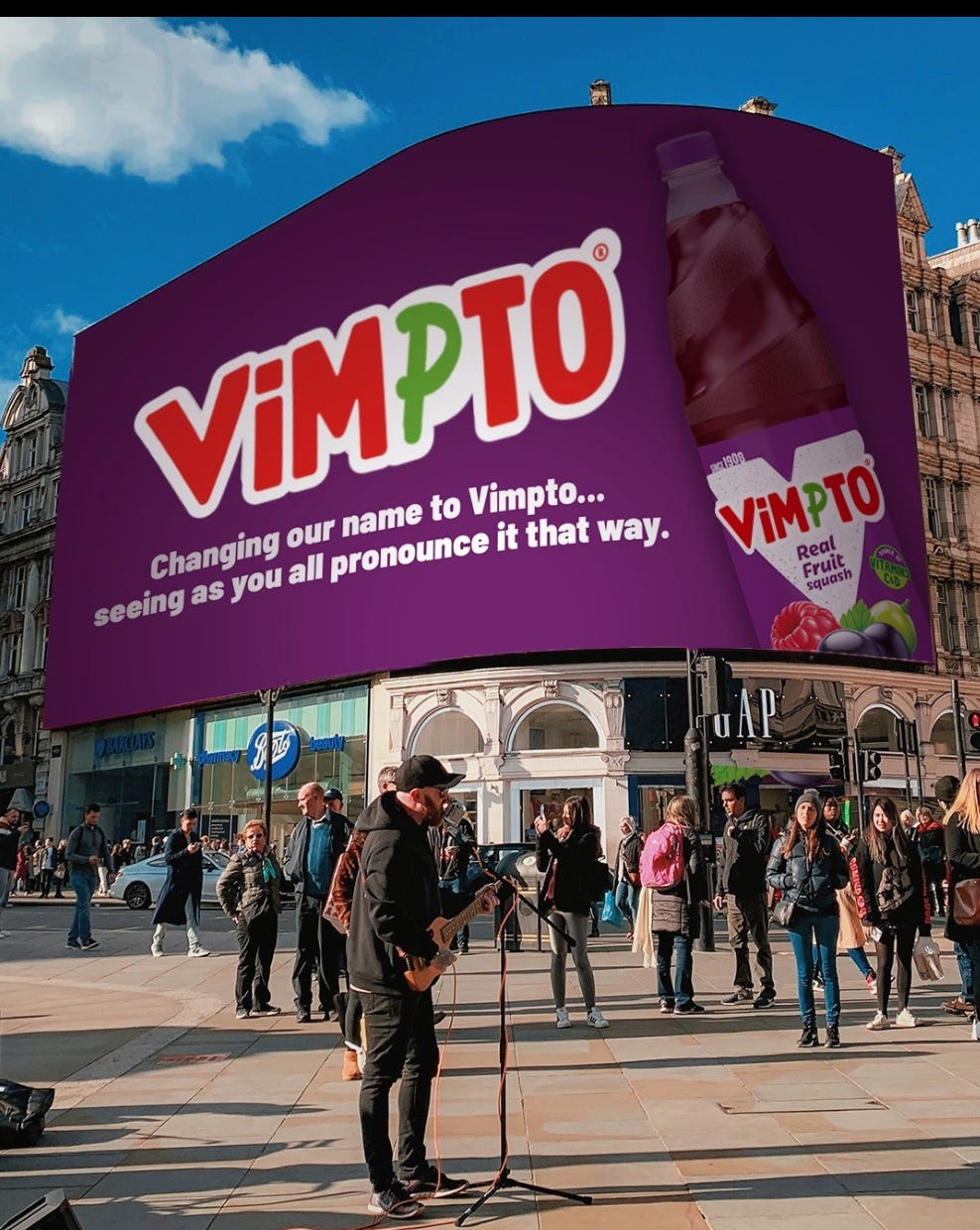 london's piccadily circus with a large billboard advertisement for Vimto, a soft drink. The billboard humorously states, "Changing our name to Vimpto... seeing as you all pronounce it that way