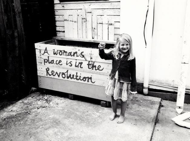 Little girl next to a sign saying "A woman's place is in the revolution"