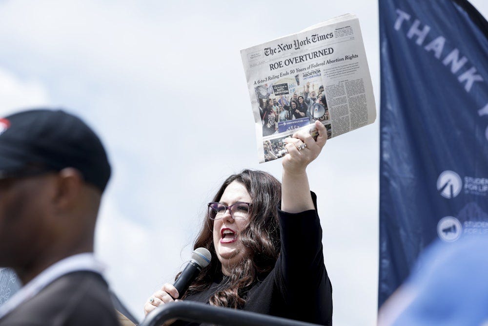 A woman holds up a copy of The New York Times reading "Roe Overturned."