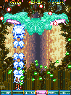 A screenshot of a boss fight from V-V, which sees smaller green bullets moving slowly toward your ship, one grazing the side (but not the hit box) of it, while red orb bullets are near the top of the screen. A third projectile is charging on the underside of the boss' wings.