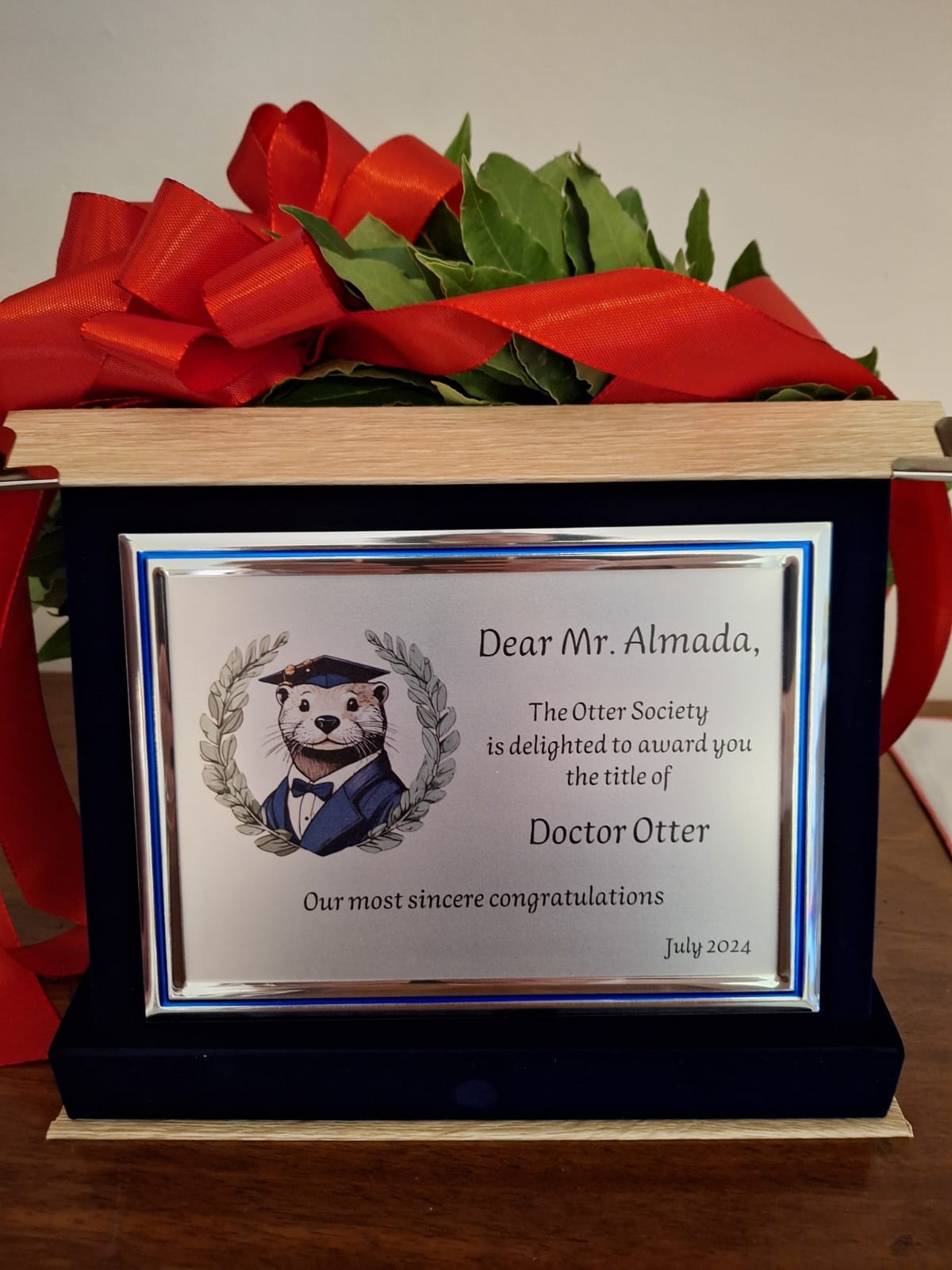 A commemorative plaque, featuring an otter in black tie and a graduation hat. The plaque says: "Dear Mr Almada,

The Otter Society is delighted to award you the title of 

Doctor Otter 

Our most sincere congratulations"