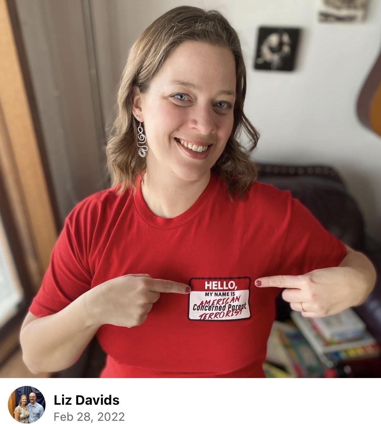 Liz Davids smiling and pointing at her shirt that says "American Terrorist"