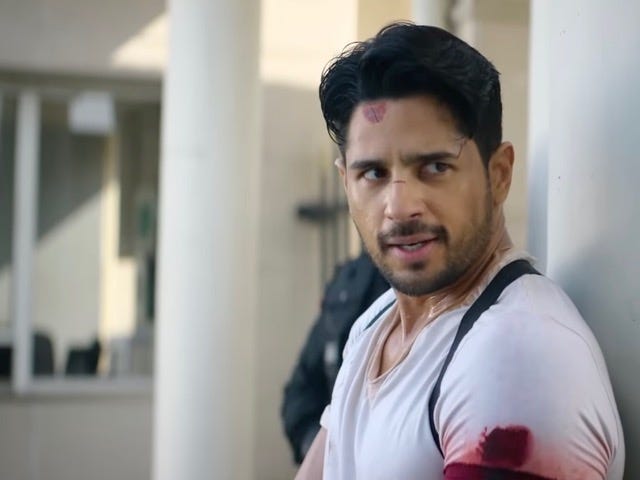 A still from Hindi film, ‘Yodha’. An injured Arun Katiyal played by Siddharth Malhotra in a white t-shirt with blood stains. Looks like he is on a lookout for enemies. The background is blurred. 