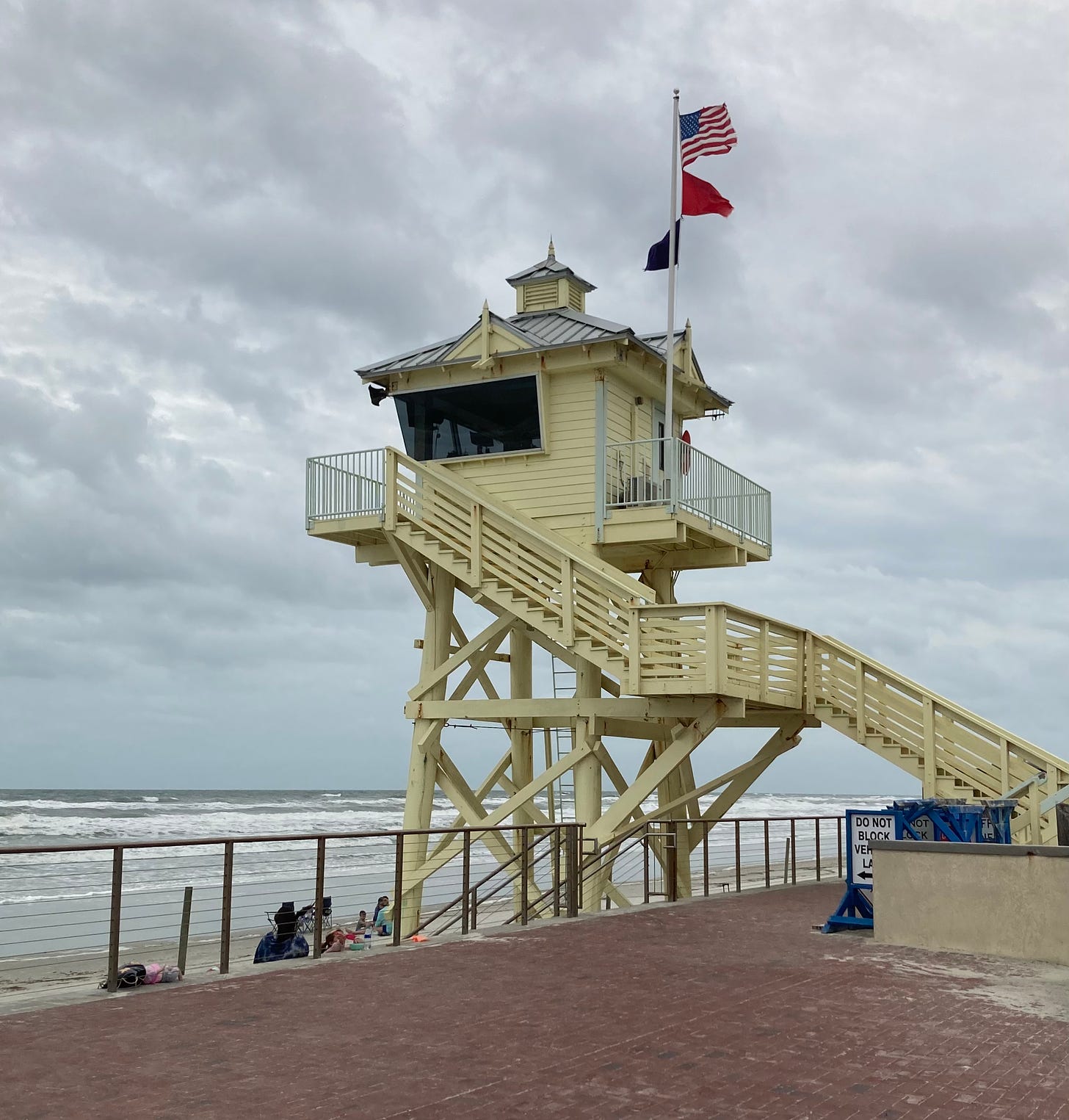 A very high, large, yellow life guard station overlooking an ocean with a rough surf. 