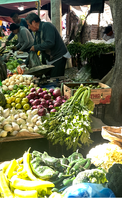 Colourful vegetable stands with a man packing some in a paper bag.