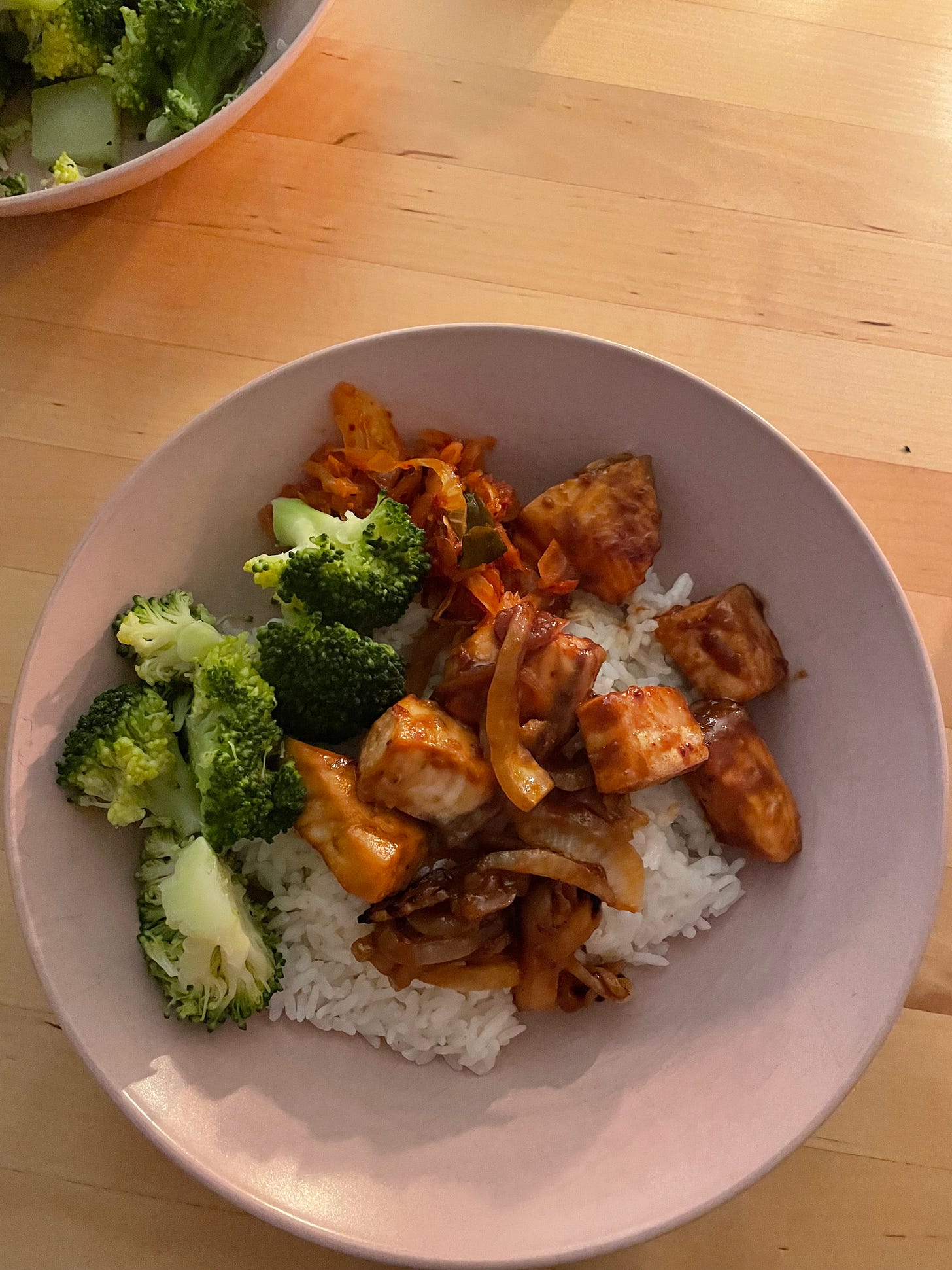 A pink bowl filled with rice, roasted cubes of salmon and steamed broccoli.