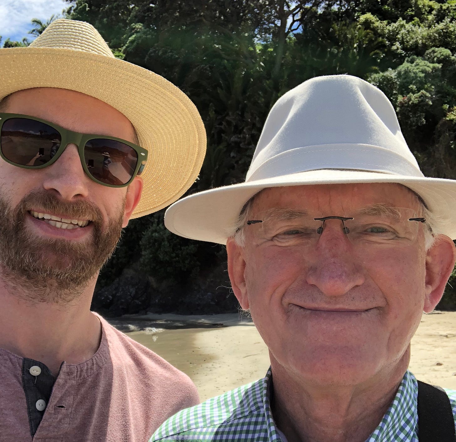 A photo of Hadley and Brian Wickham on a beach in NZ. They're both wearing sun hats and are smiling.
