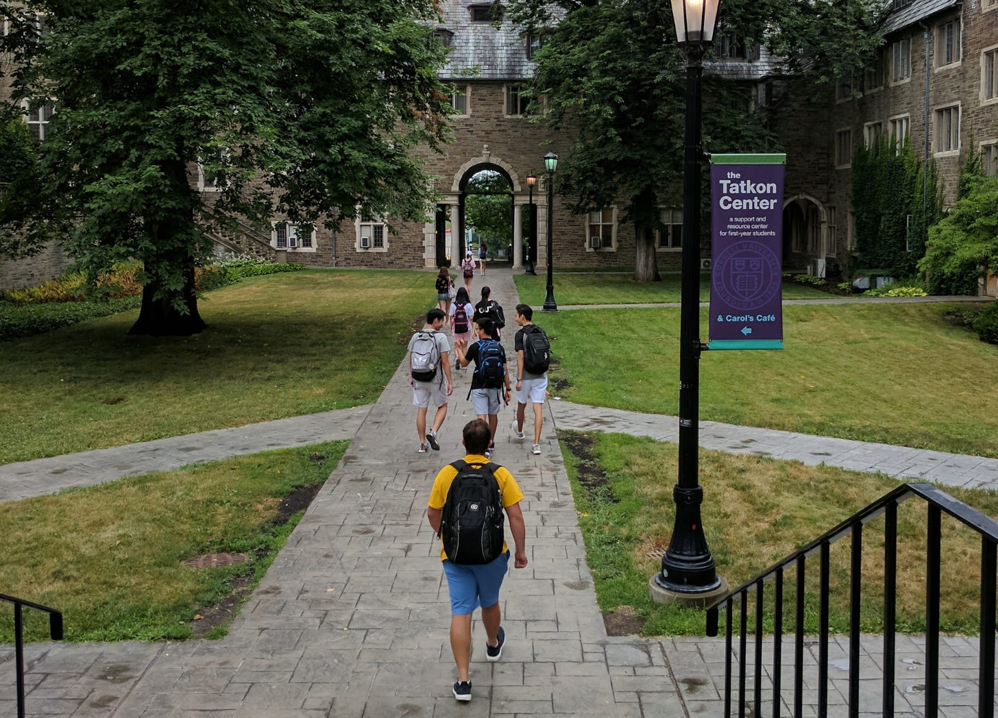 View from behind several students as they walk through a courtyard toward an archway.