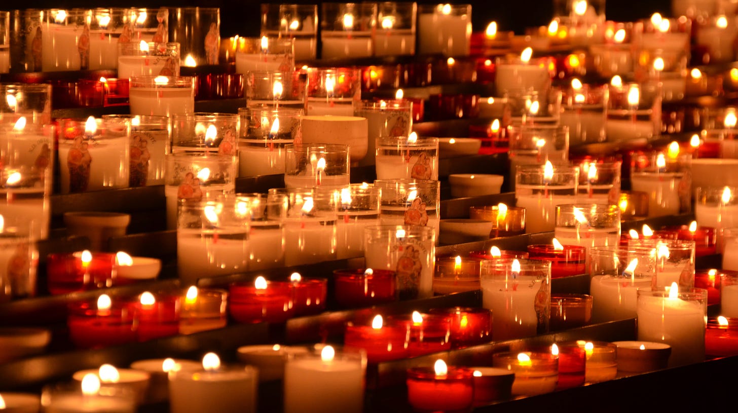 Row after row of small votive candles in white and red. They burn, pushing away the darkness.