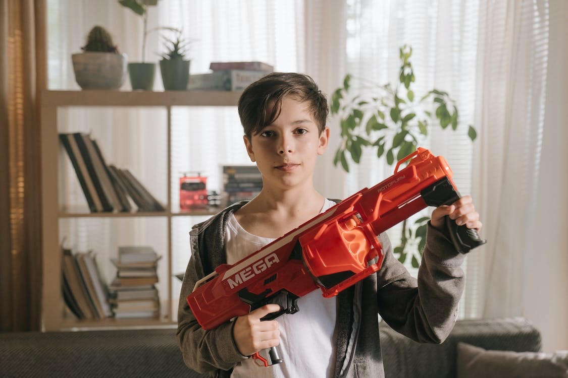 Free Boy in Gray Sweater Holding Red Plastic Toy Gun Stock Photo