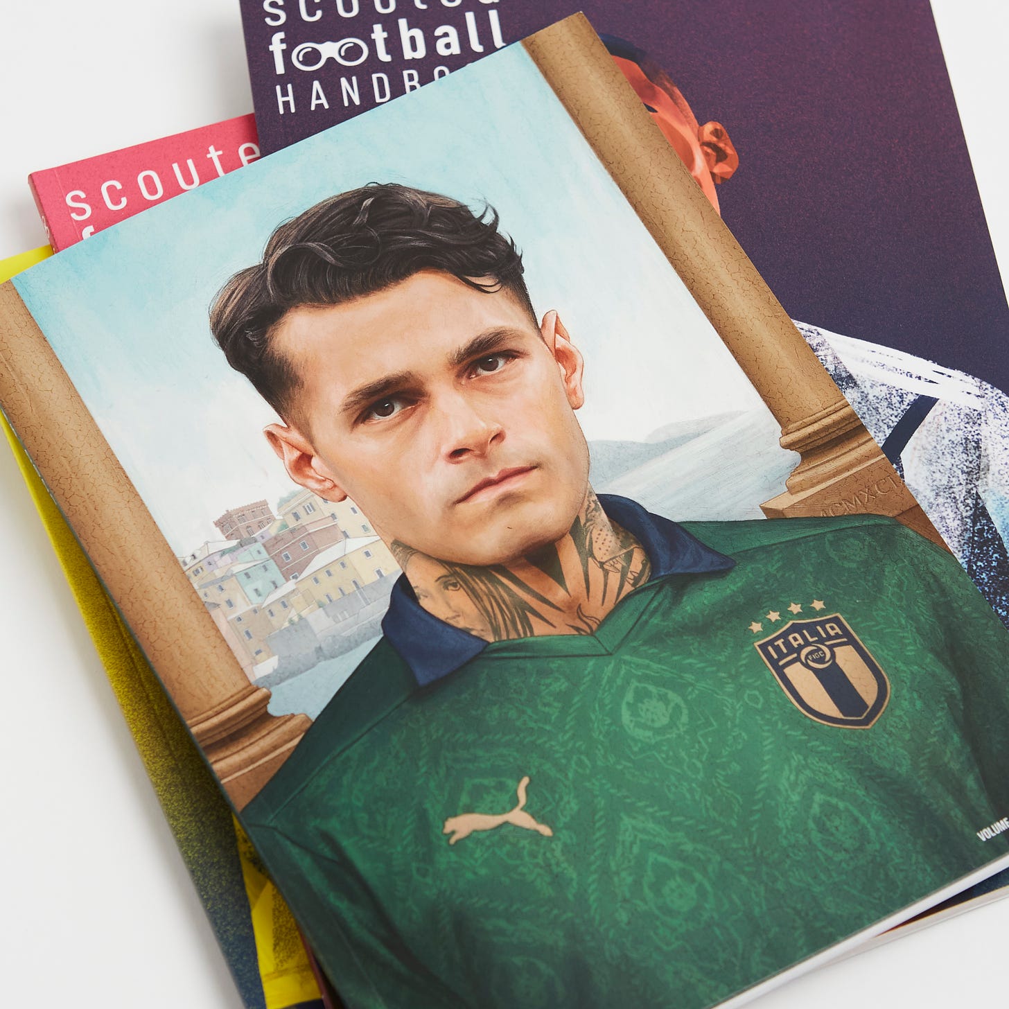 A close-up photo of a selection of classic Scouted Football Handbook editions, featuring a portrait photo of Gianluca Scamacca in a renaissance-inspired Italy kit