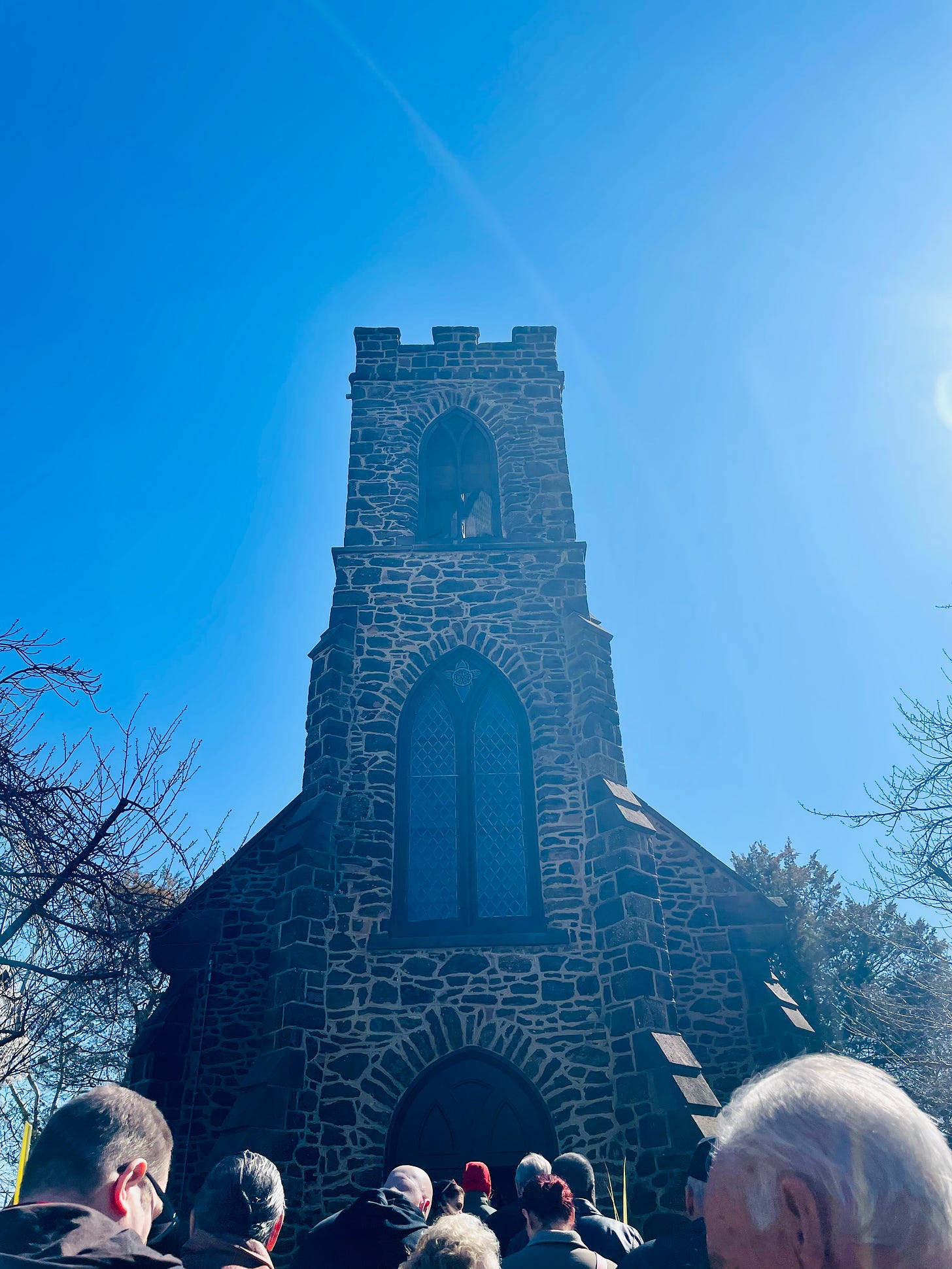 A brick church against blue sky, a few heads in the bottom of the frame, processing into the church.