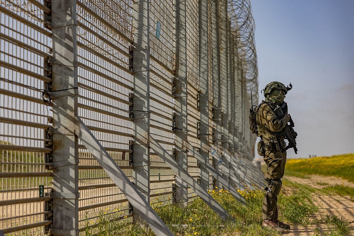 An Israeli soldier stands next to the fence encircling the Gaza Strip, March 18, 2025. (Chaim Goldberg/Flash90)