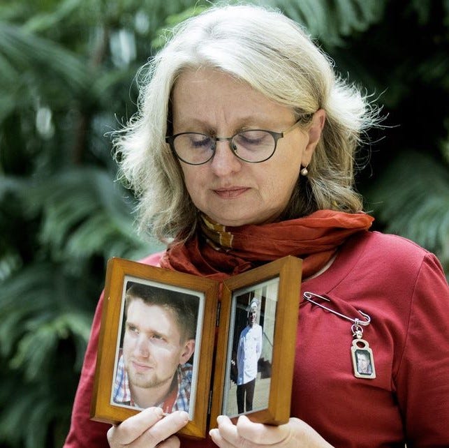 Petra Schulz — Moms Stop The Harm holds framed photos of her deceased son Danny while looking downward at them