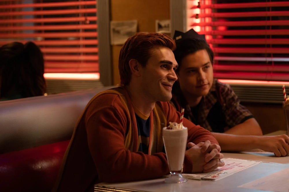 A red-headed boy and another boy sit at a diner with a milkshake