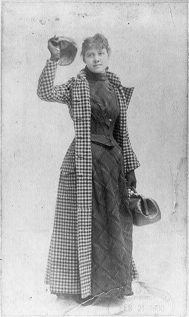 Photograph of Nellie Bly in her traveling outfit. She is carrying one small bag.