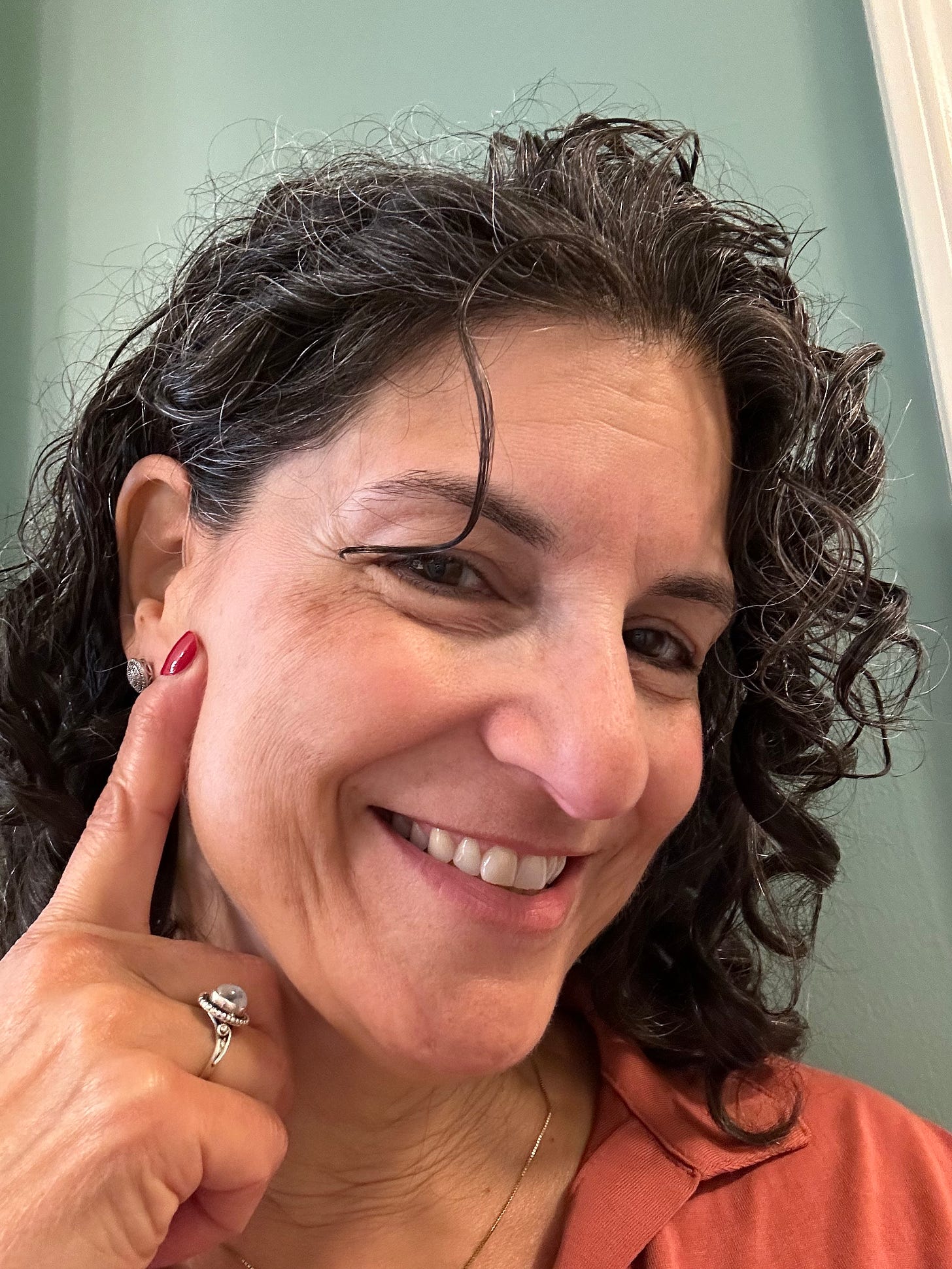 Dark-haired woman pointing to her hearing aid