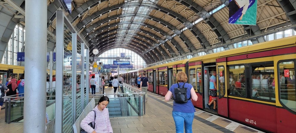 A yellow and red S-bahn train pulls into the station at Berlin's Alexanderplatz transit station. Passengers begin to disembark.