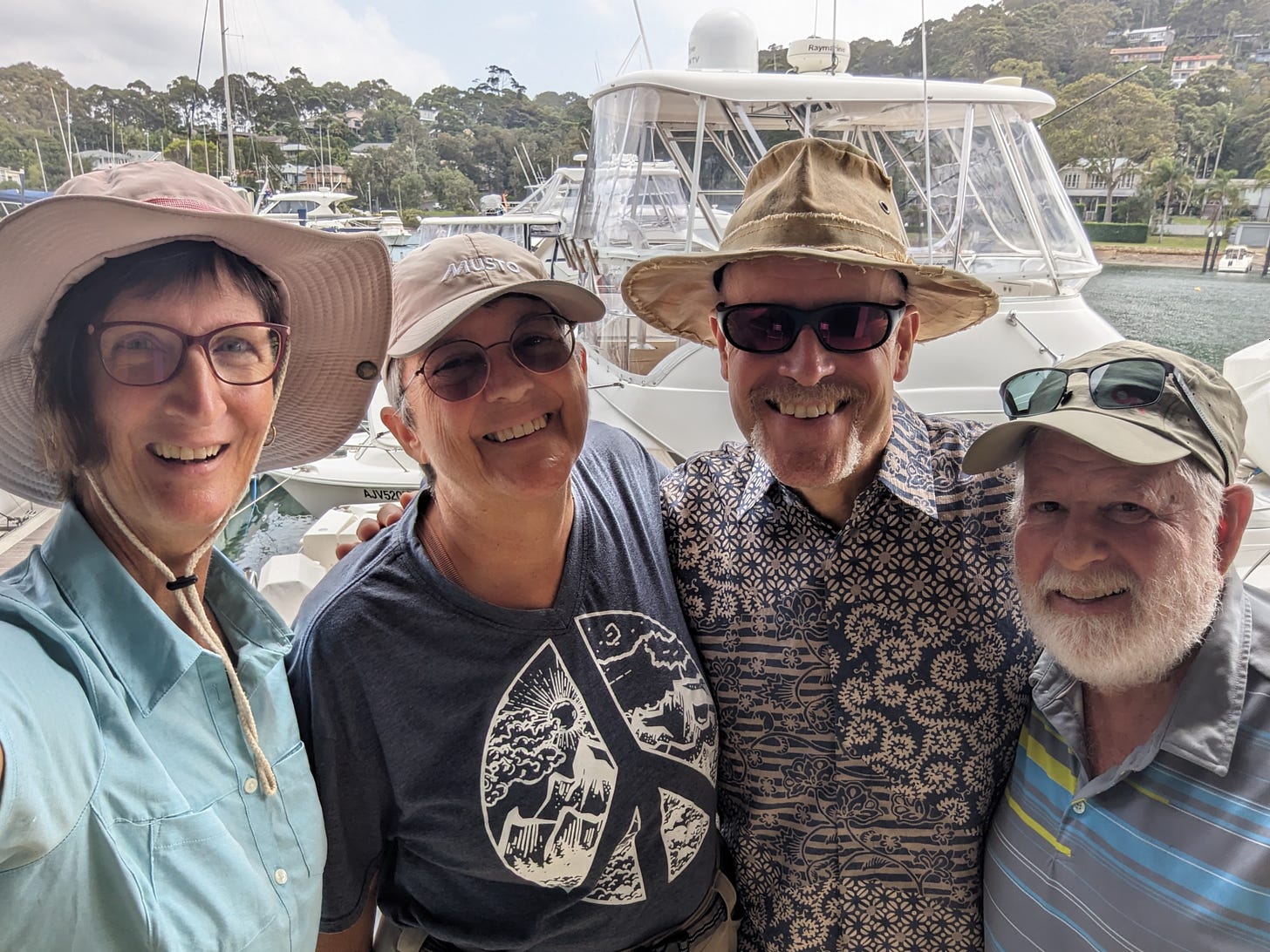 Sherry, Robbie, Andy, and Gene, arms around each other, smiling for the camera in a marina with boats all around