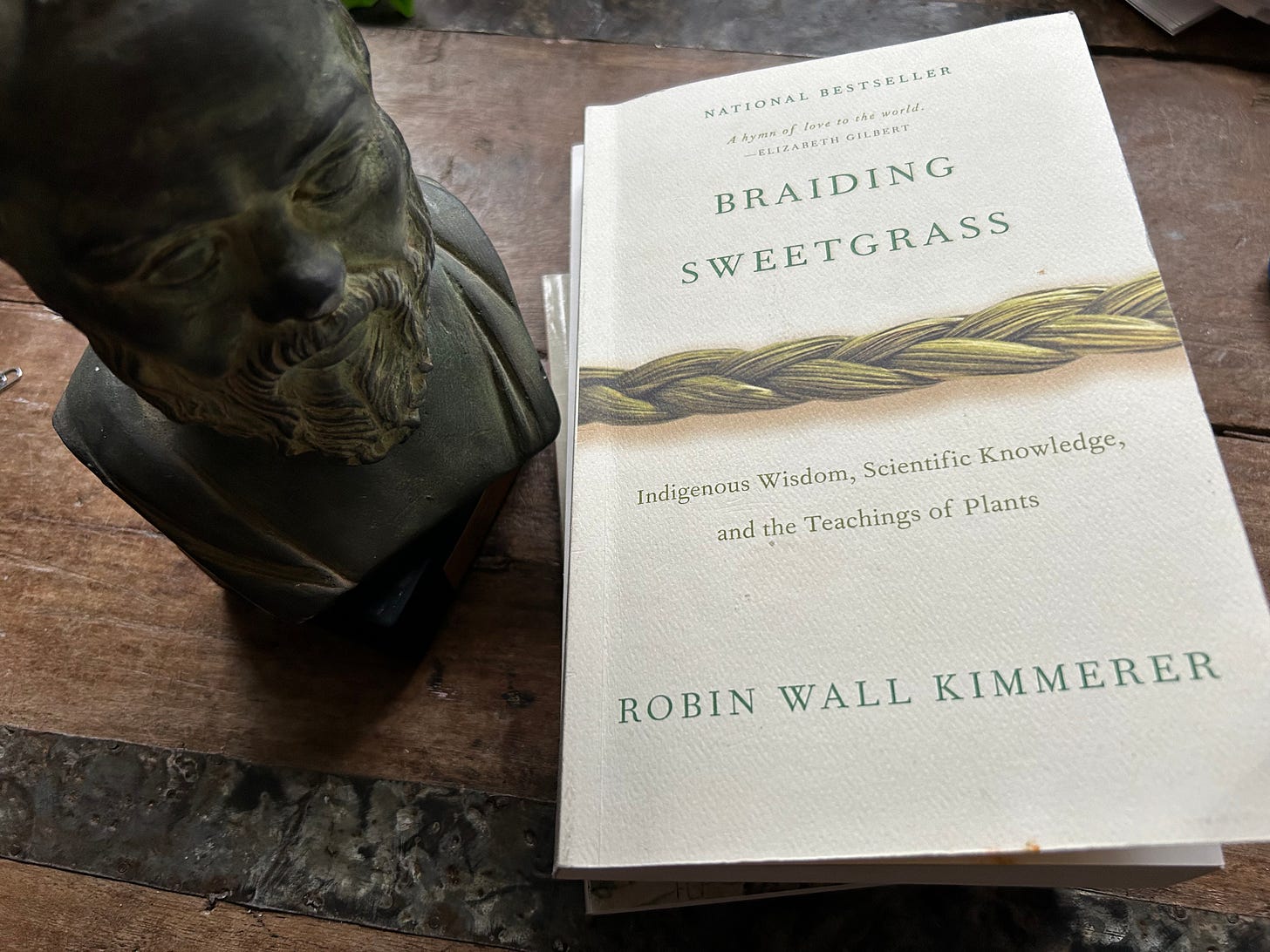 A bronze statue of the philosopher Socrates looms over a copy of Robin Wall Kimmerer's book Braiding Sweetgrass.