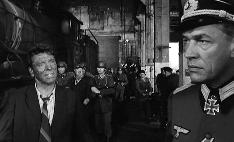 Still from The Train (1964) showinf a grease smeared train engineer (Burt Lancaster) pleading with a Nazi general in a huge train hangar.