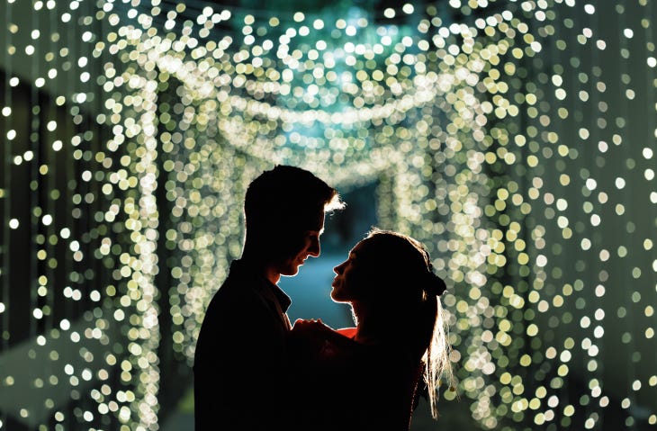 Two people silhouetted in front of a tunnel of fairy lights