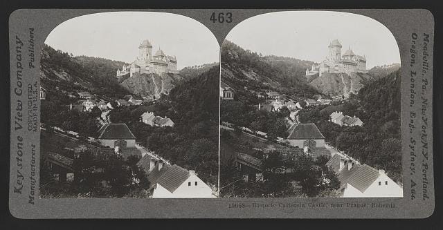 a black and white image of a small village in a valley with a castle in the background