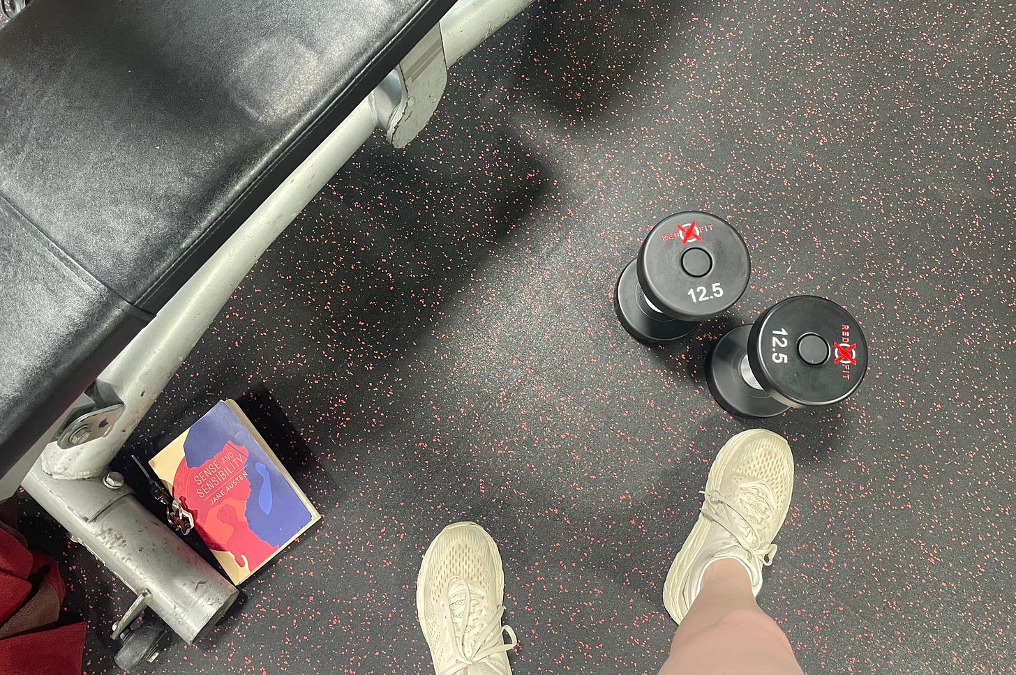 Image of the ground with a book, an exercise bench, and two 12.5-lb dumbbells 