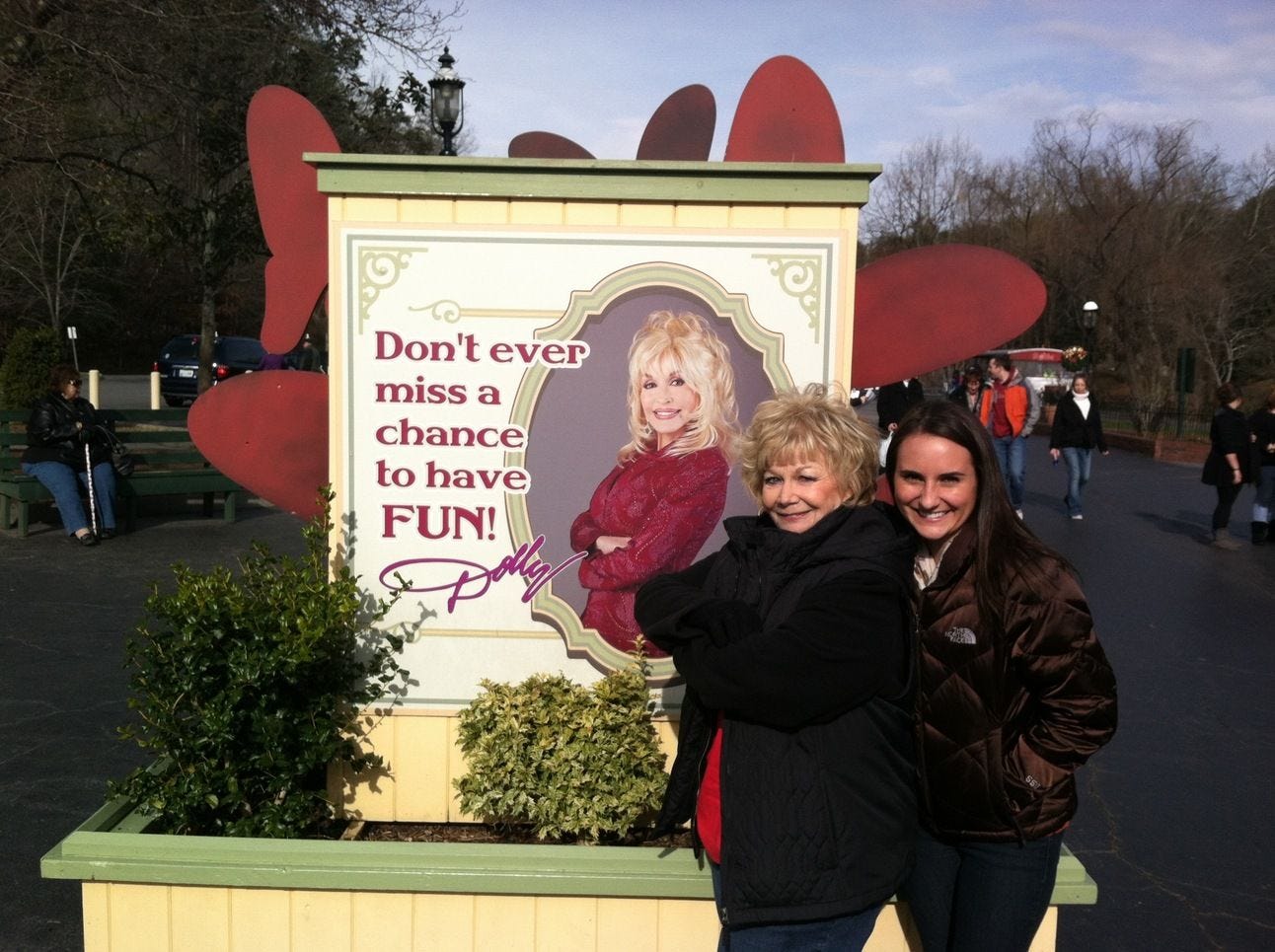 two women standing in front of a Dolly Parton sign two women standing in front of a Dolly Parton sign