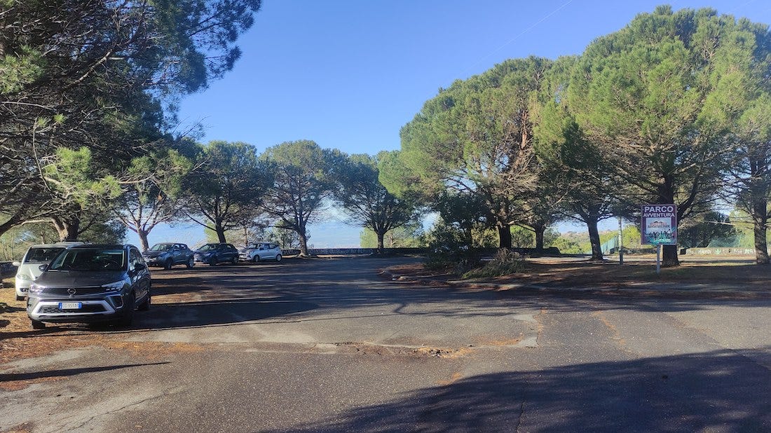 Large tarmac parking area surrounded by trees with a view down the hill