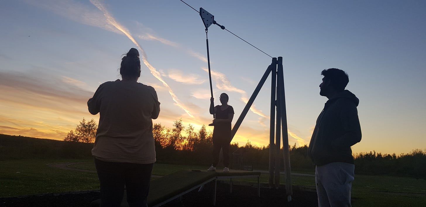 Silhouettes of three adults against the sunset playing on a zipwire