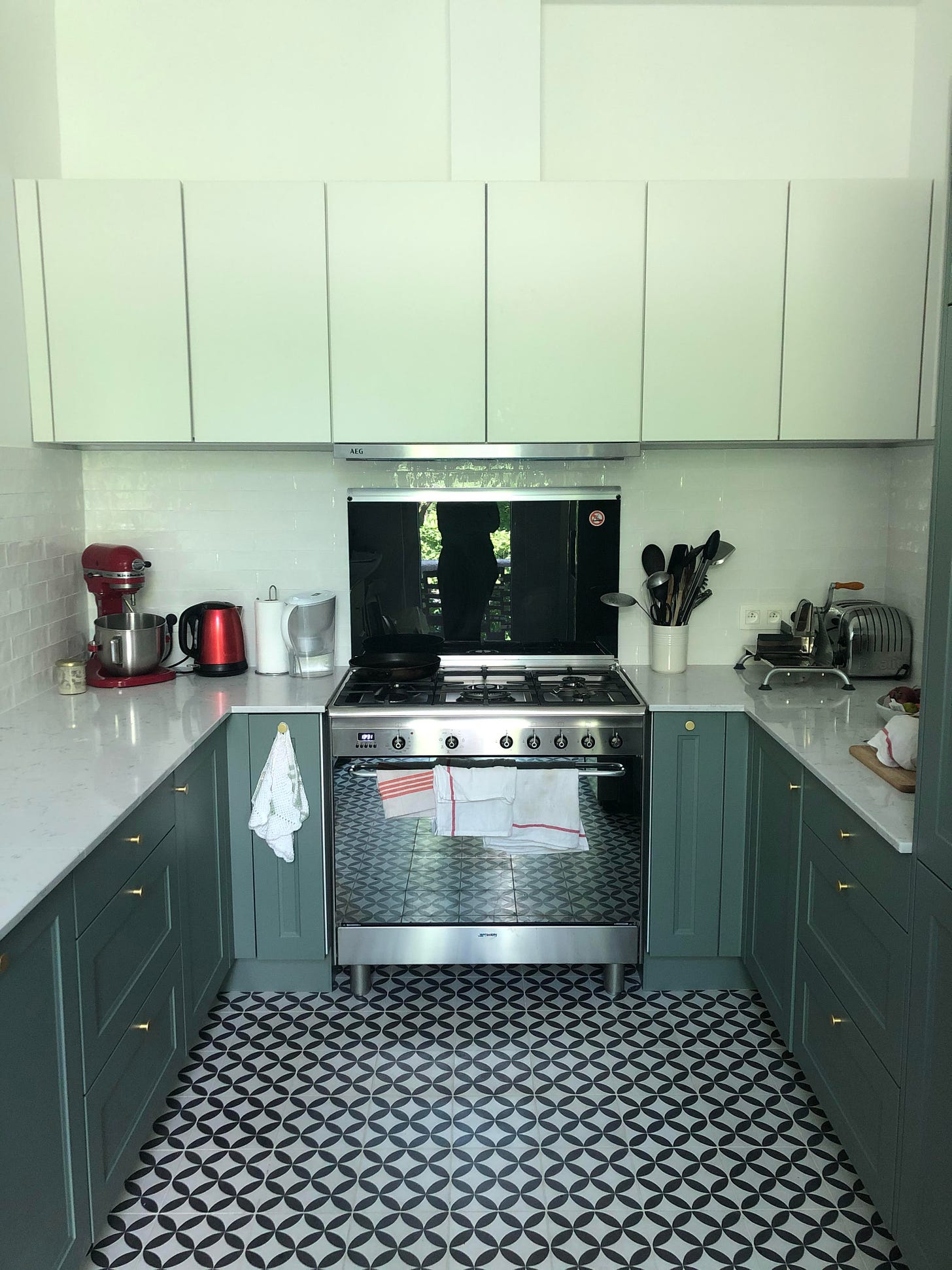 Bright mint green kitchen with grey coloured cupboards and large stove.