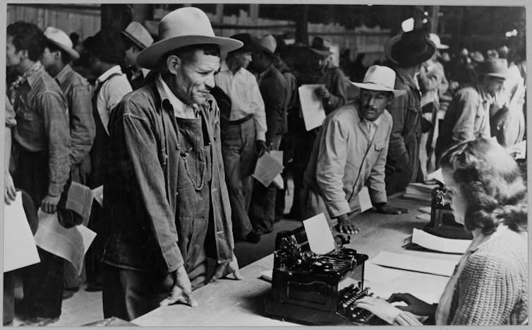 A black and white image of a Mexican farm worker indoors with his hands on a table.