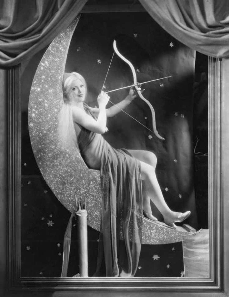 This may contain: an old photo of a woman sitting on the moon with a bow and arrow in her hand