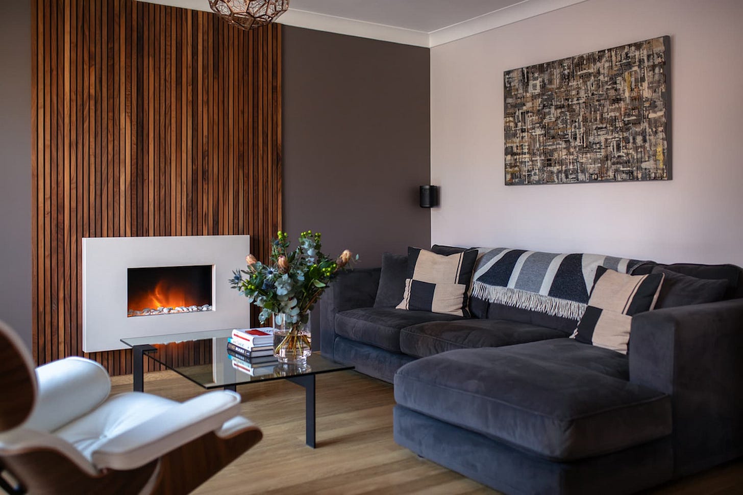 Modern living room with walnut feature wall and marble electric fire positioned in the centre with grey corner sofa and modern glass coffee table