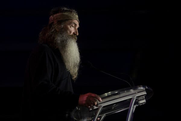 A man with a long white beard standing at a lectern.