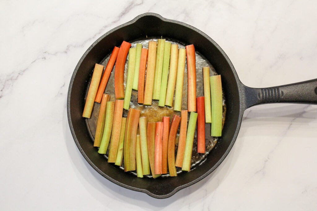 Prepared cast iron pan with caramel and cut rhubarb on a light background.