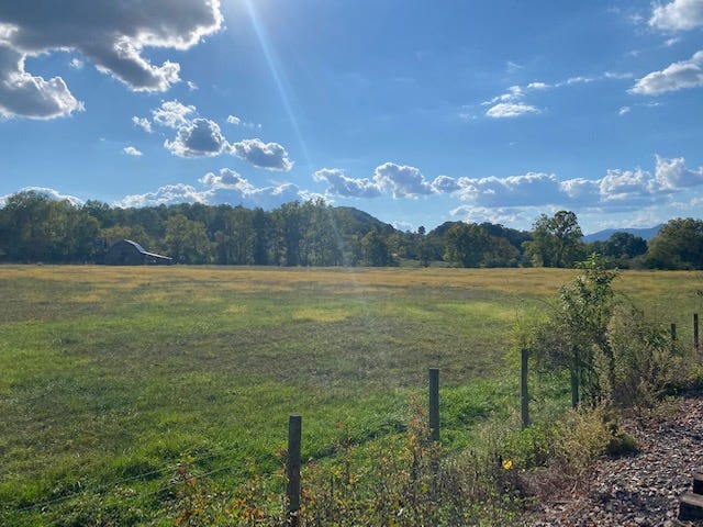 pasture with a barn and rolling hills under a blue sky with a few clouds