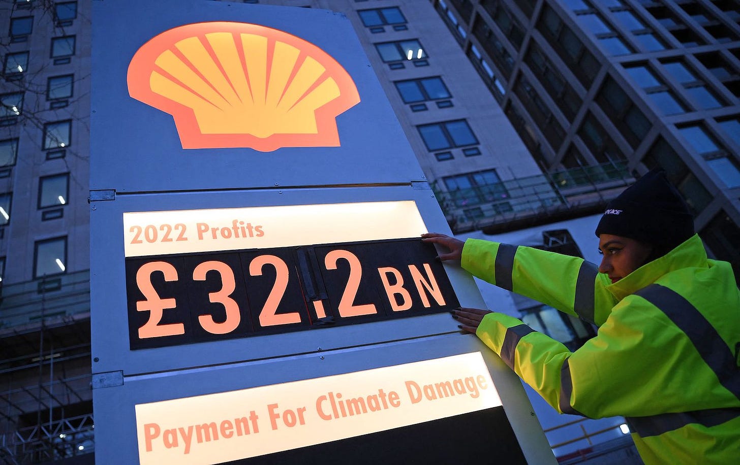 A woman in a yellow safety jacket adjusts numbers on a Shell gas station logo. The numbers read: 2022 profits, 32.2 billion pounds, payment for climate damages zero.