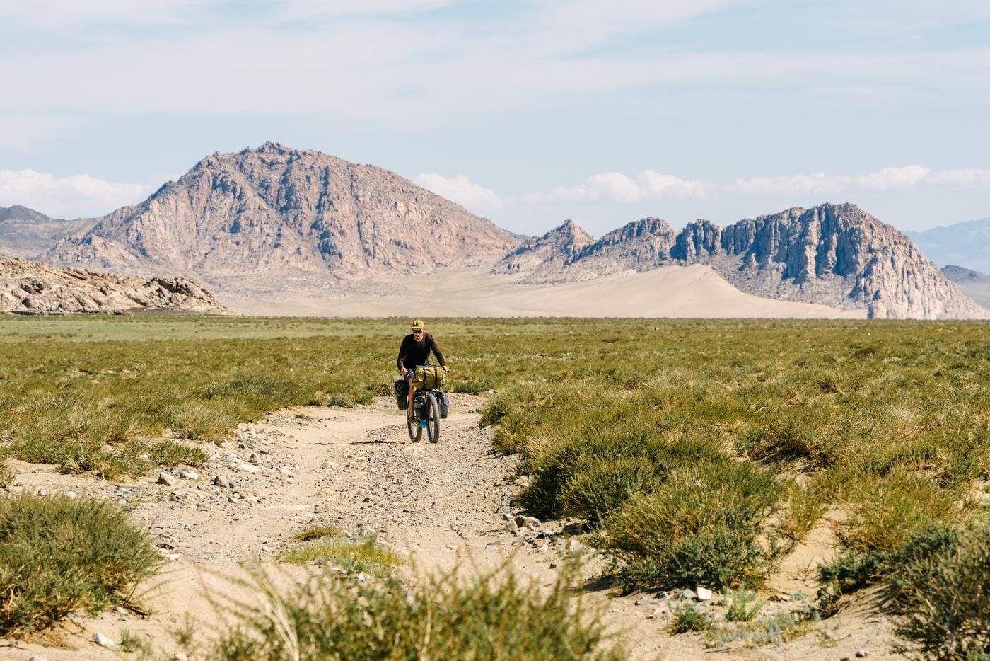 Voyageur a velo au milieu d'un desert avec les montagnes derrieres.