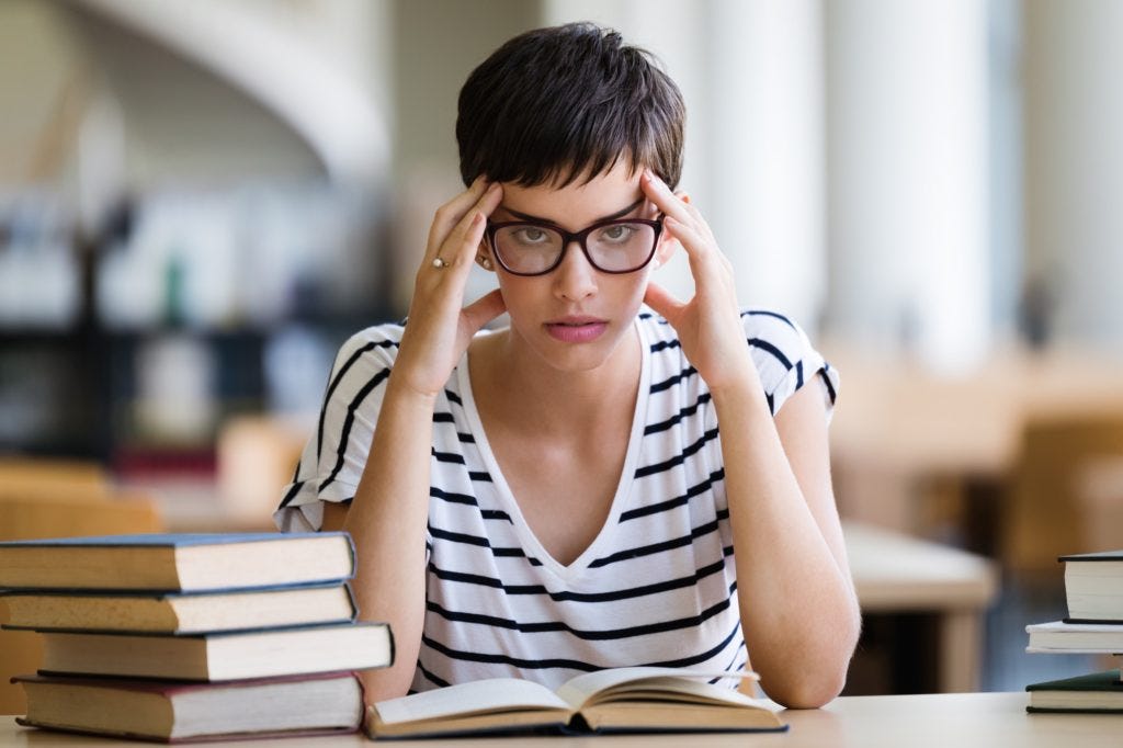 Young stressed student girl studying pile of books