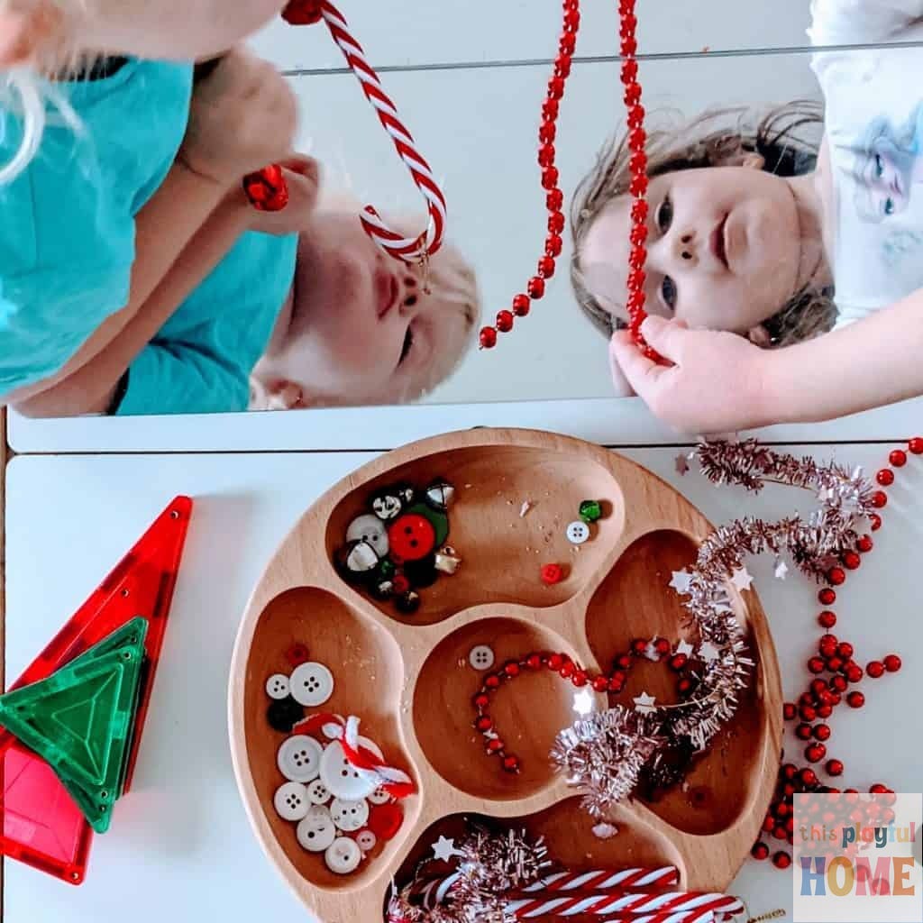 two young children explore christmas decorations by placing them on a mirror