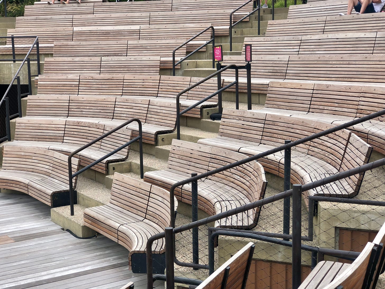 An amphitheater, curved seats of pale wooden slats, black metal handrails dividing sections of the seating.