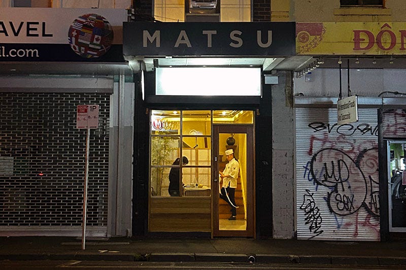 A store front with the name 'Matsu' above it. Two people stand inside.